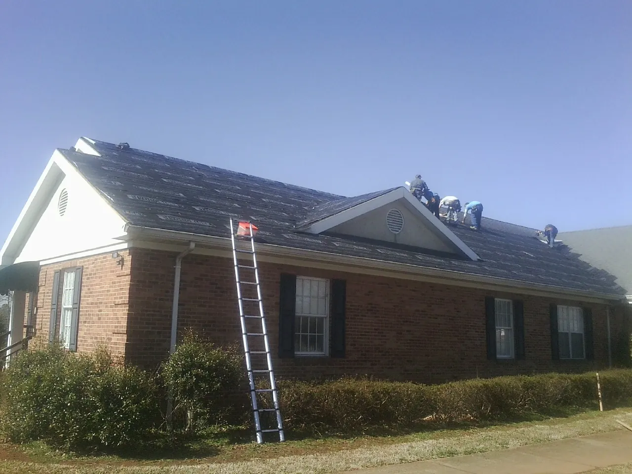 Crew tearing shingles off a brick ranch roof with a ladder set — Metal Roof Repair work by our crew in Oldtown