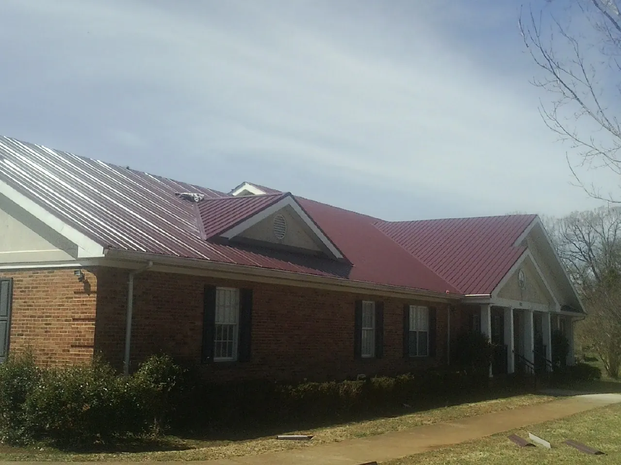 Red metal roof with gabled entries on a long brick building, from a Hail Damage Roof Repair job in Oldtown