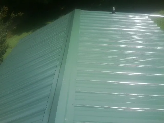 New green metal panels meeting at the ridge of a roof — Flat Roof Repair work by our crew in Oldtown